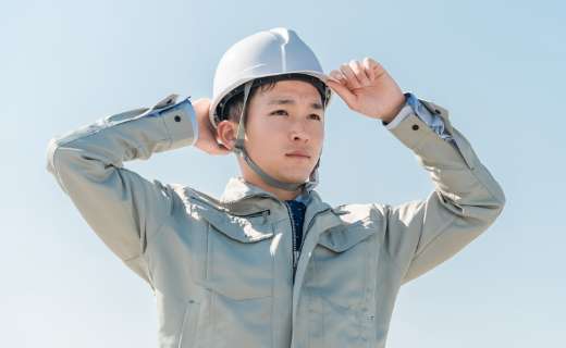 白いヘルメットを被ってグレーの作業着を着ている作業員の写真